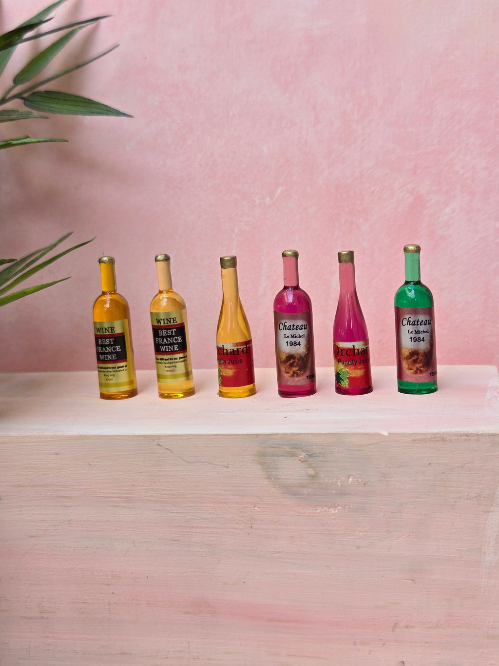 Six small bottles of Chateau 1904 wine on a white surface with a pink background