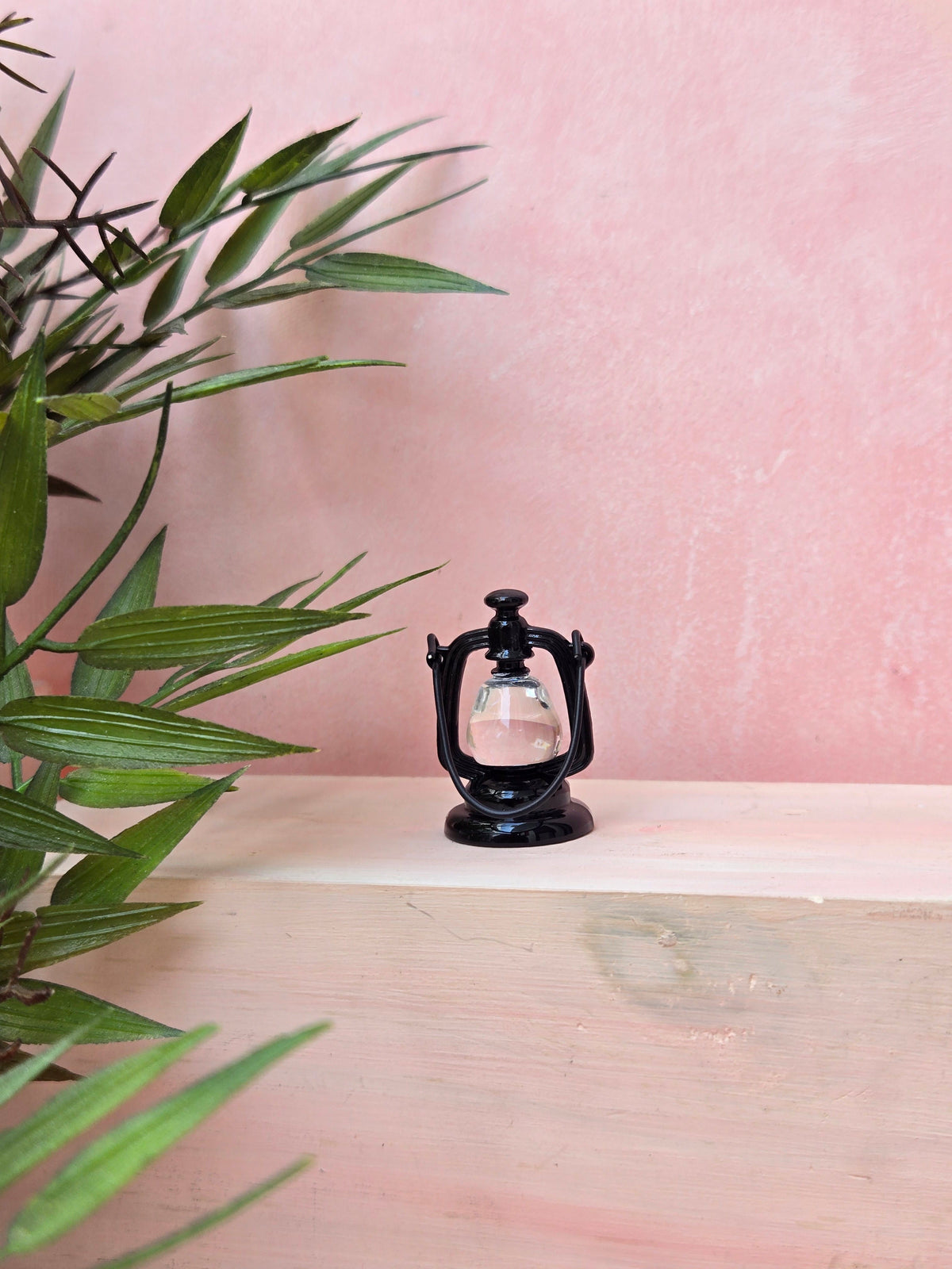 Black lantern on a wooden surface with a pink textured wall in the background