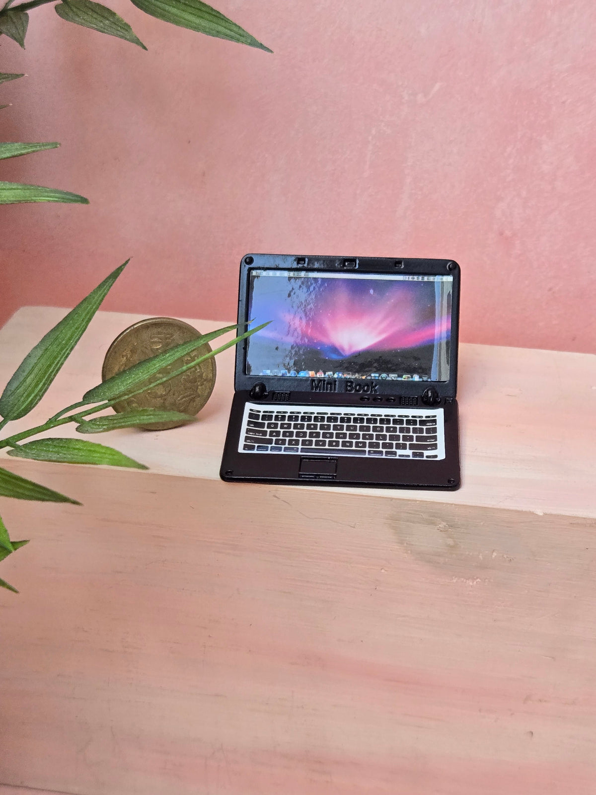 Small laptop on a wooden surface with a pinkish background