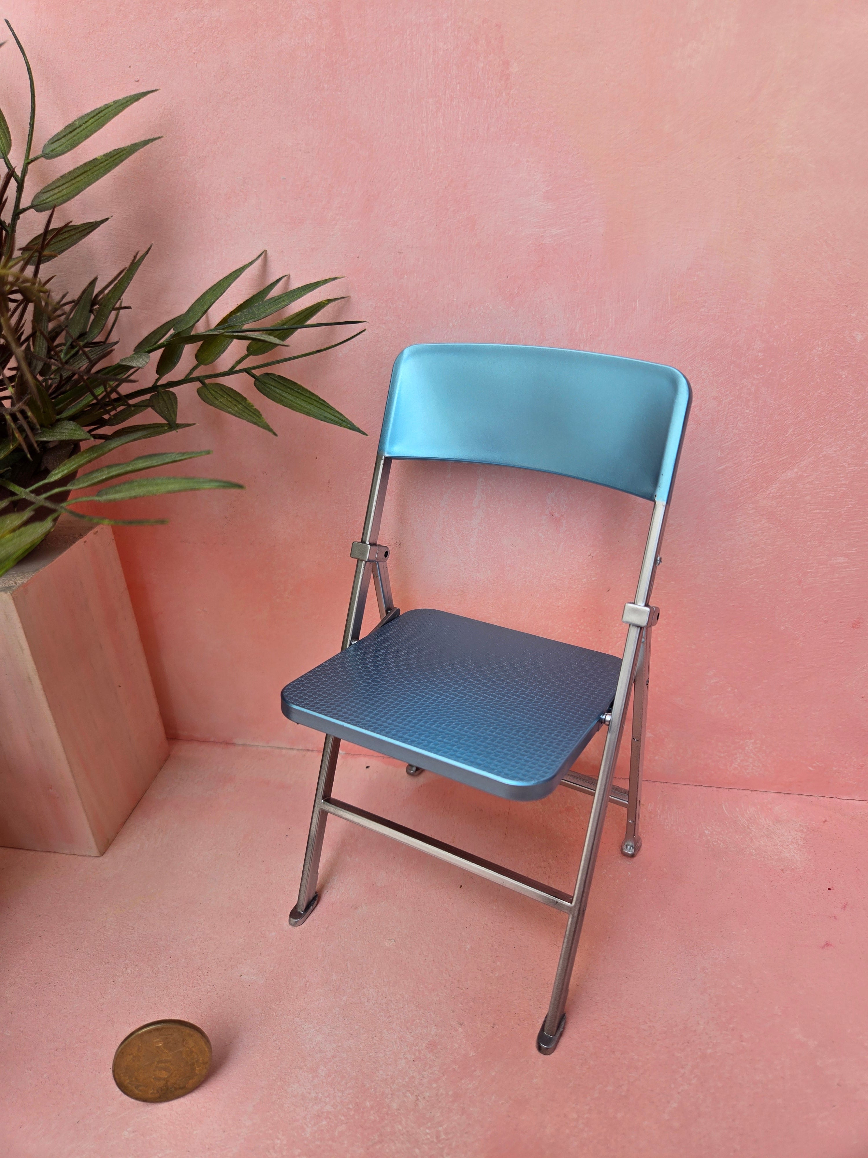 Blue folding chair on a pink floor with a plant in the corner