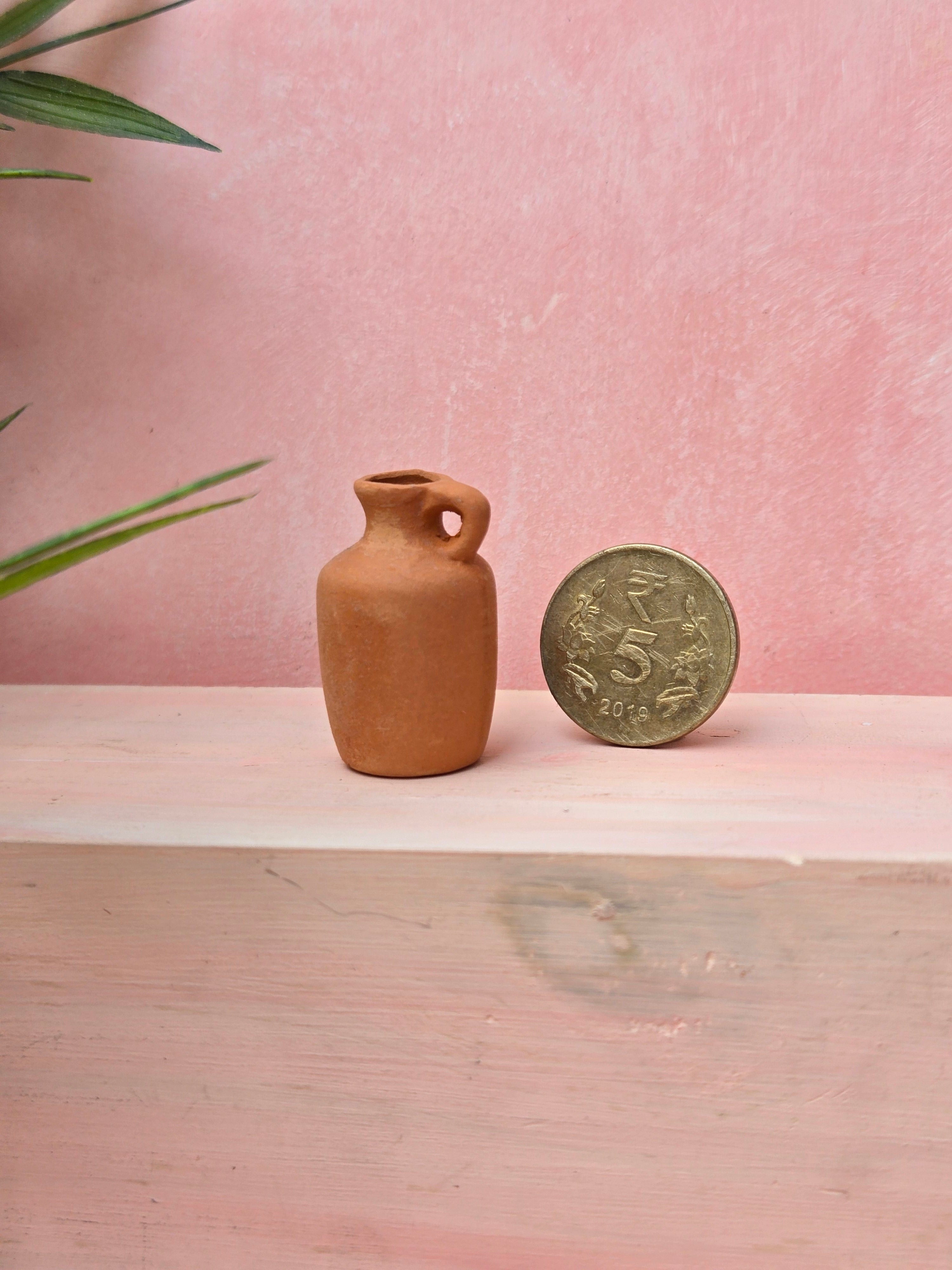 Small terracotta vase next to a coin on a wooden surface with a pink background