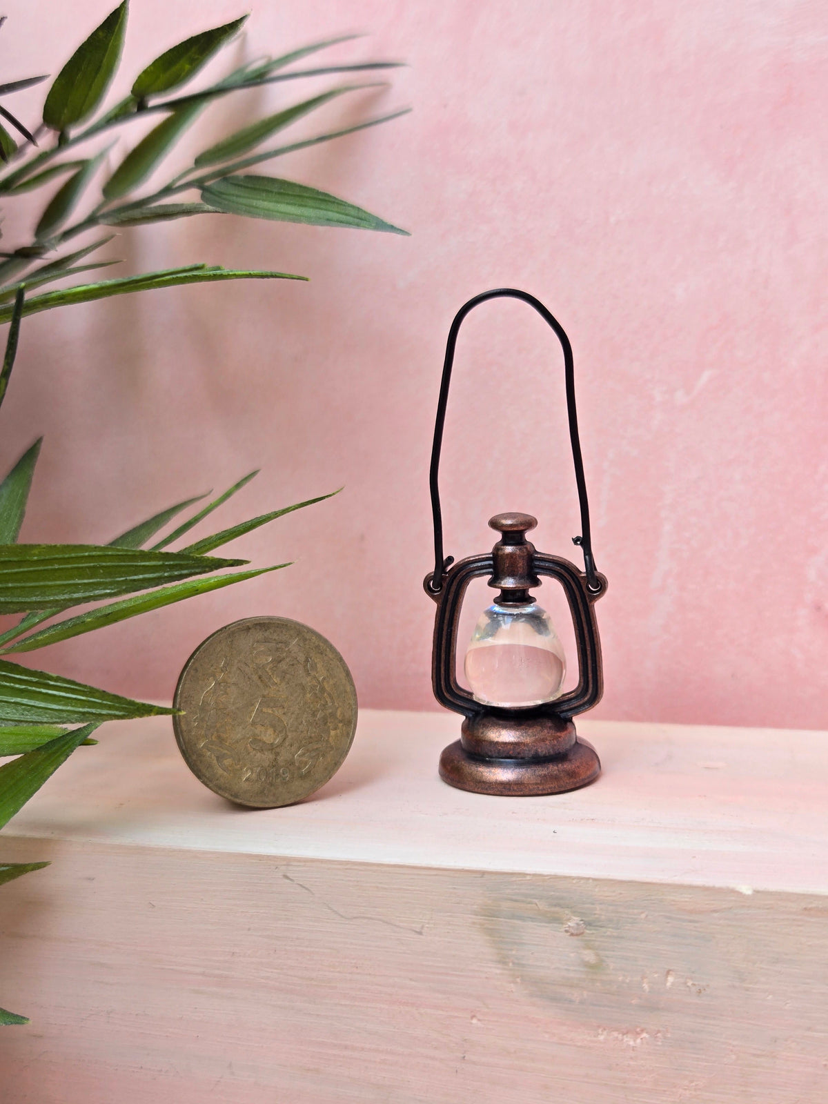 Vintage-style oil lamp on a wooden surface with a pink background