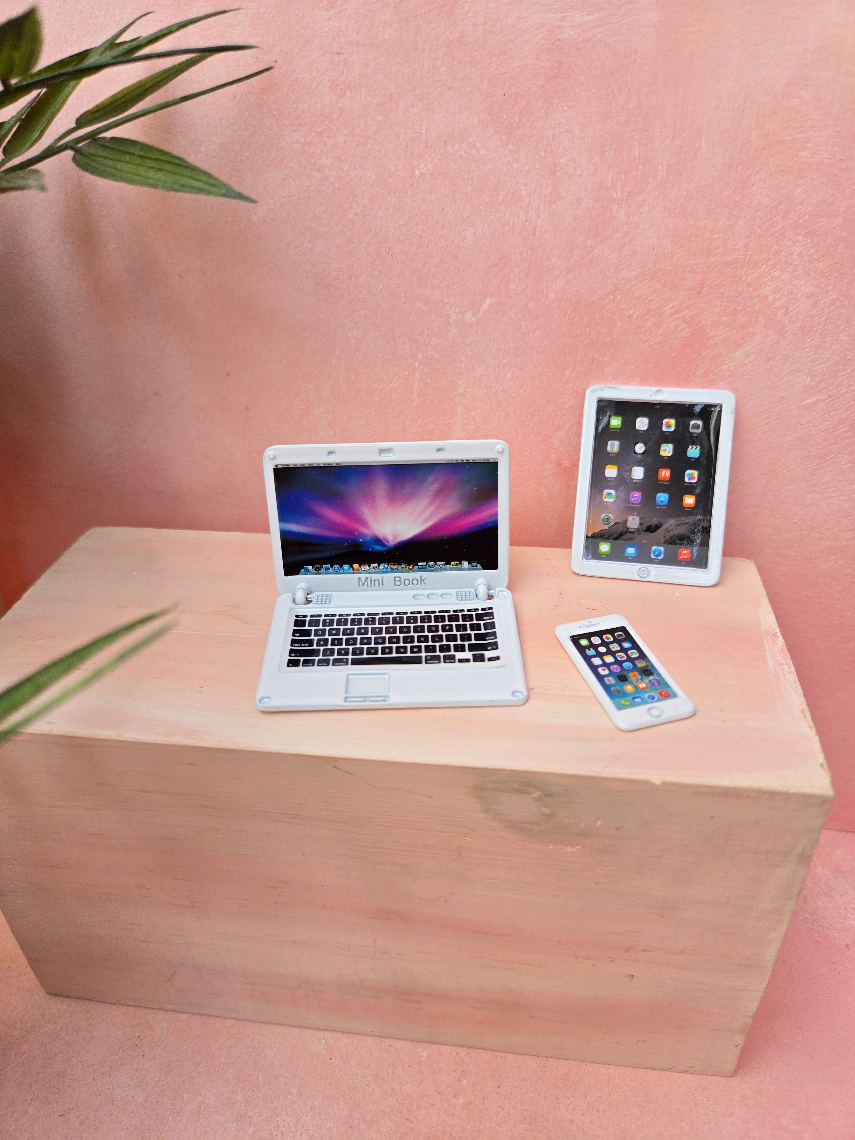 Laptop, tablet, and smartphone on a wooden surface with a pink background