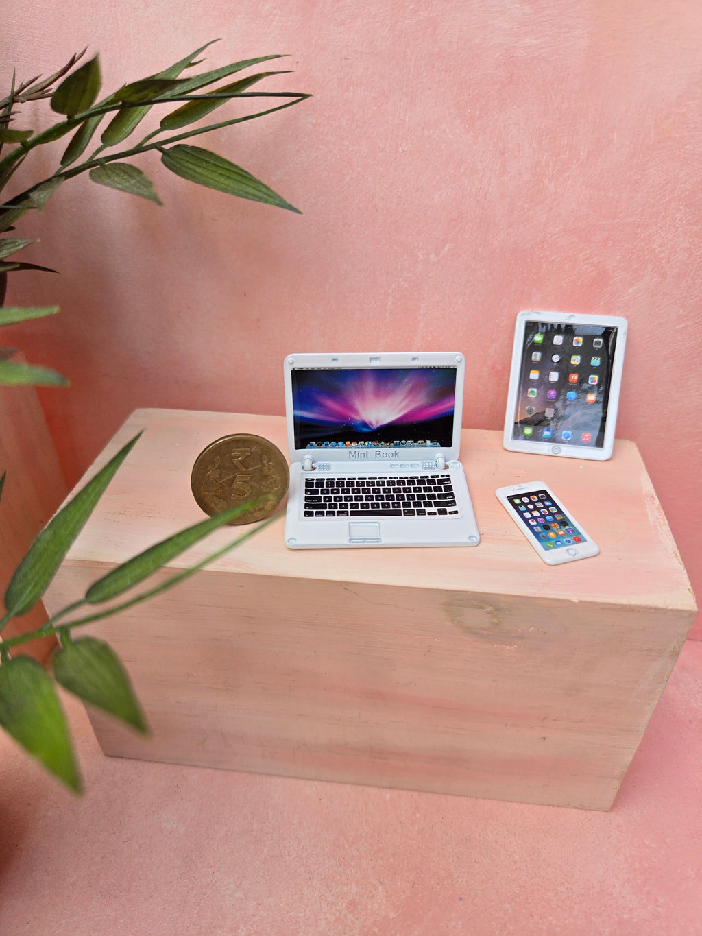 Small wooden desk with a laptop, tablet, and phone on a pink background