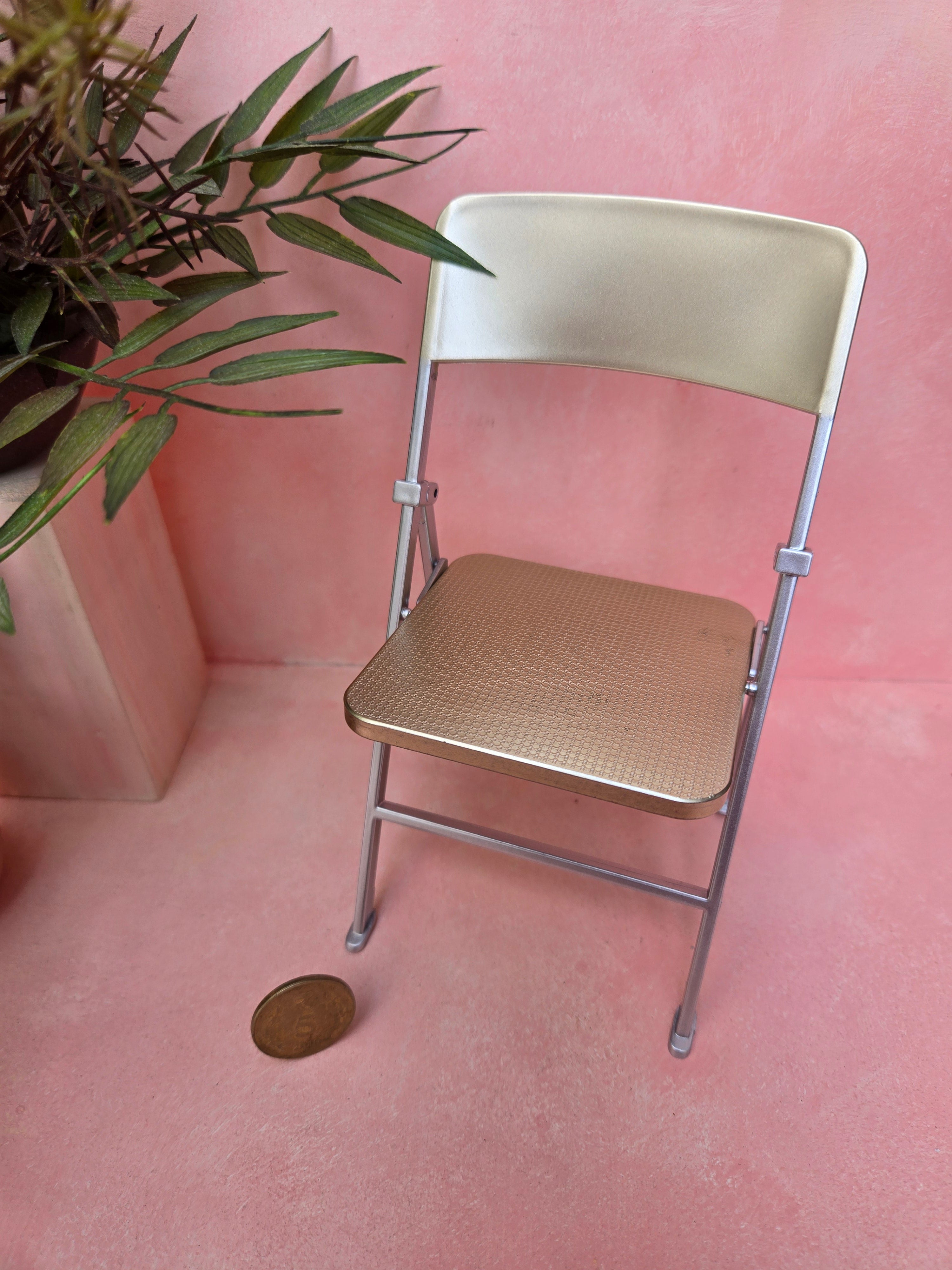 Metal folding chair on a pink floor with a plant in the corner