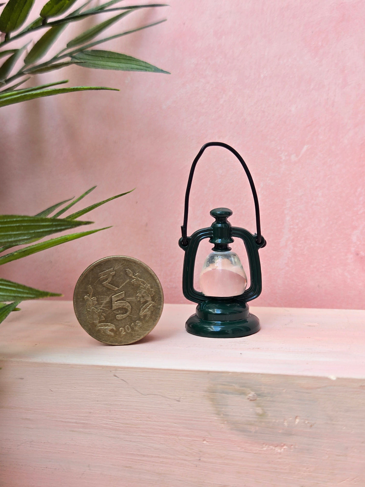 Small black lantern next to a coin on a wooden surface with a pink background