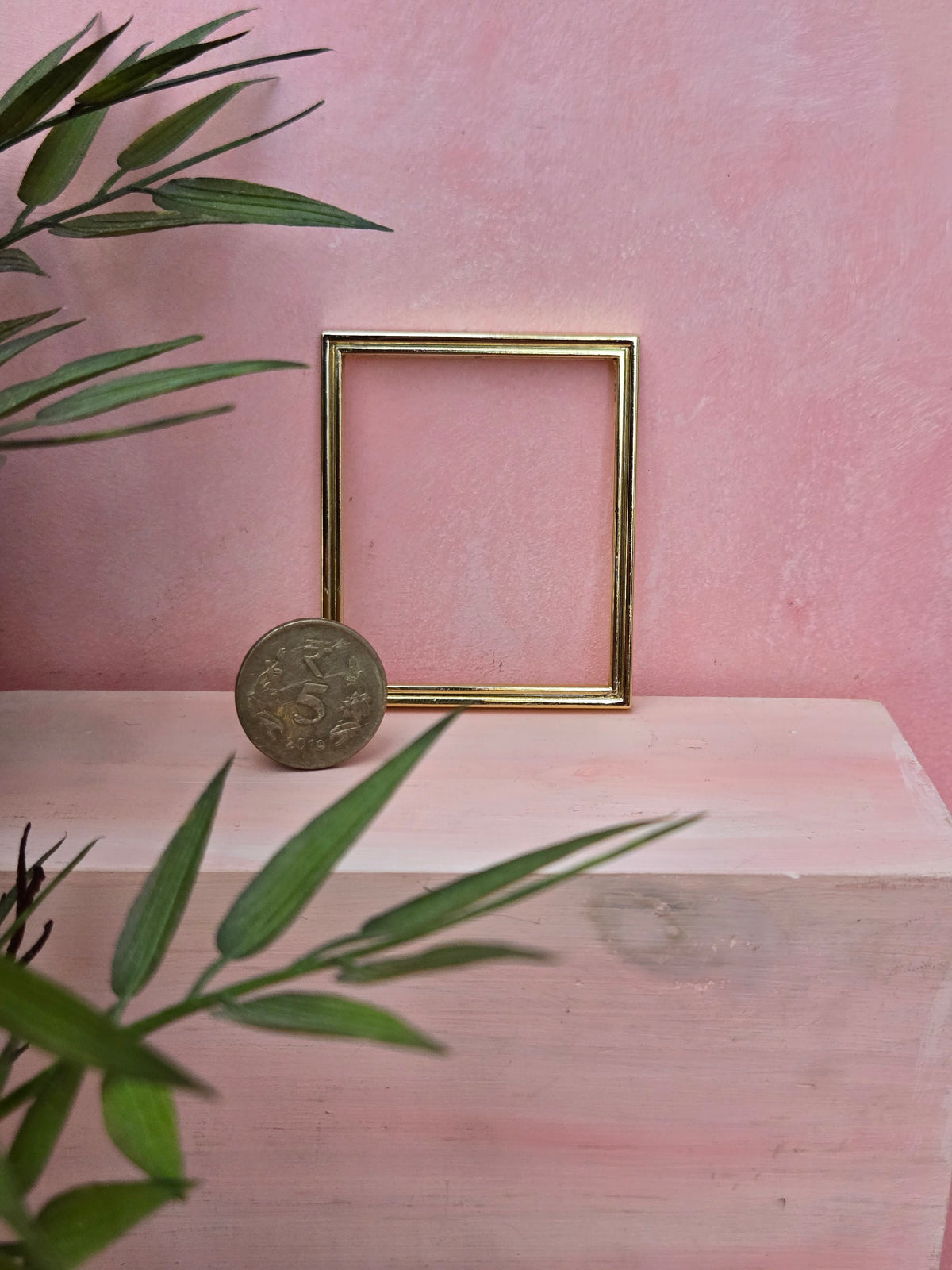 Gold picture frame on a pink surface with green leaves