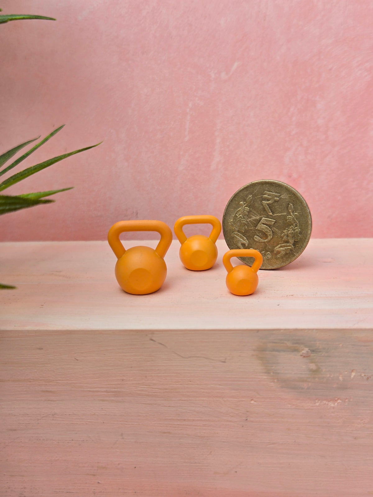 Three yellow kettlebells and a coin on a wooden surface with a pink background
