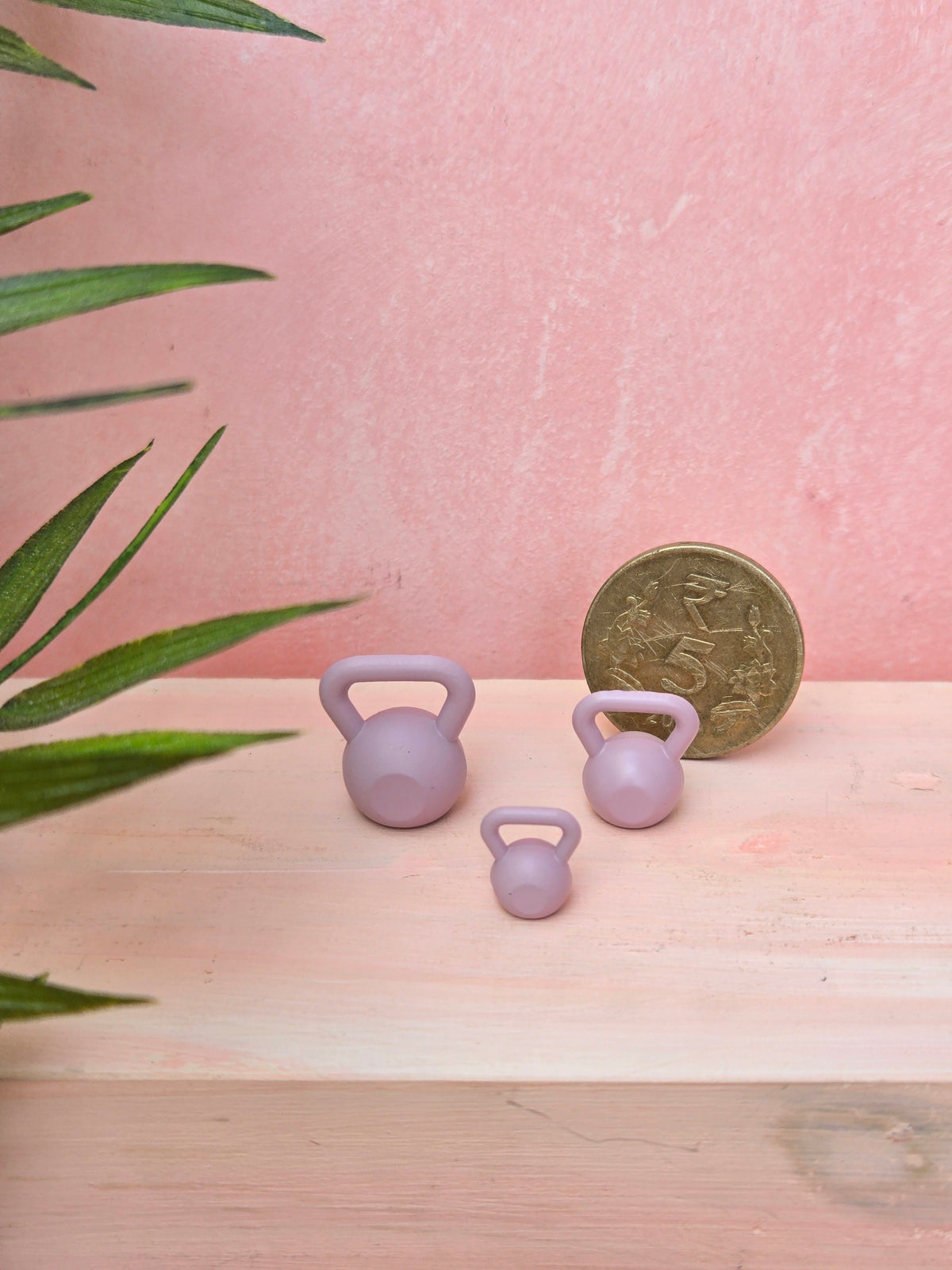 Three small purple rubber duckies on a wooden surface with a pink background and a coin for scale.