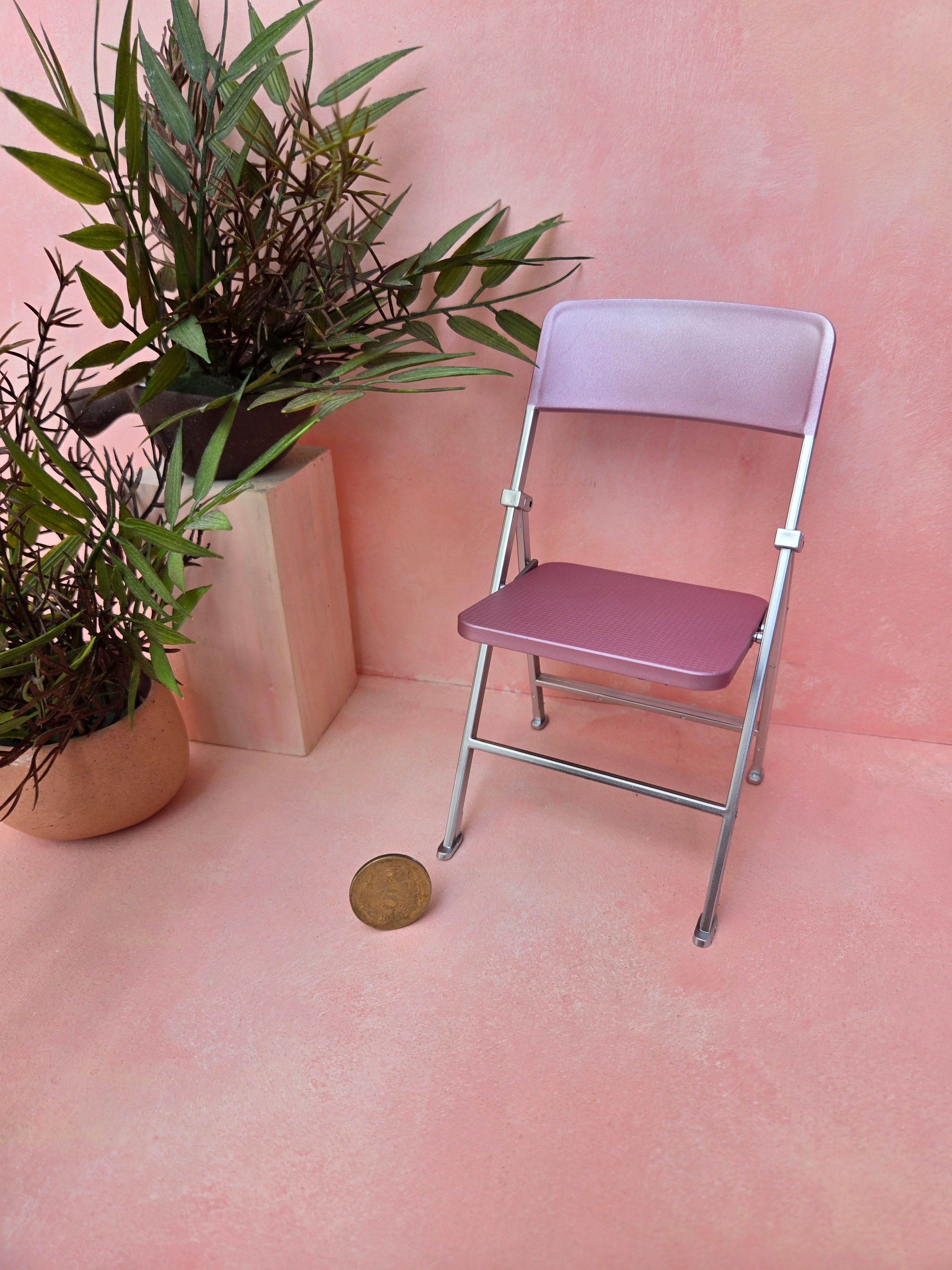 Pink folding chair next to a plant on a pink background