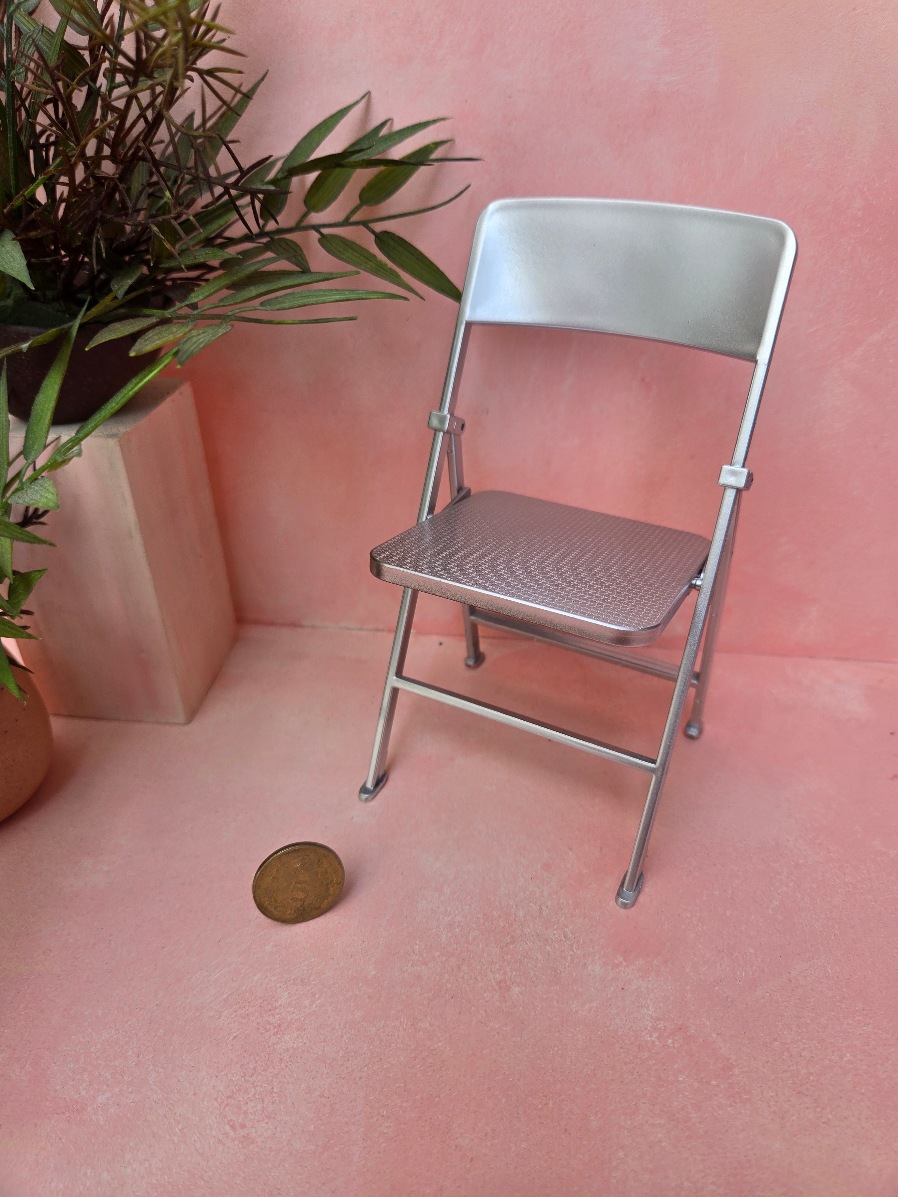 Metal folding chair on a pink floor with a plant in the corner
