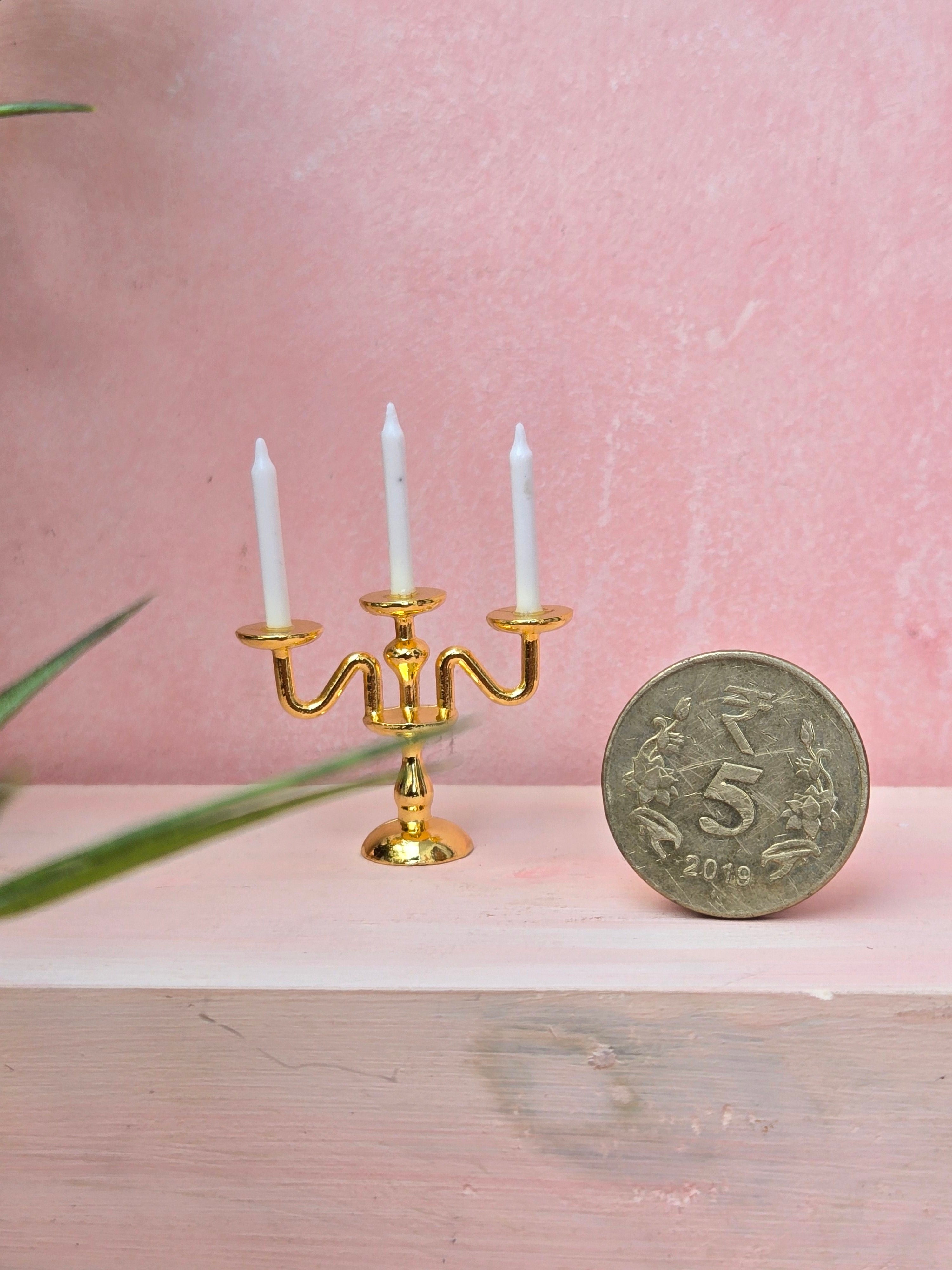Gold candelabra with white candles next to a coin on a pink background